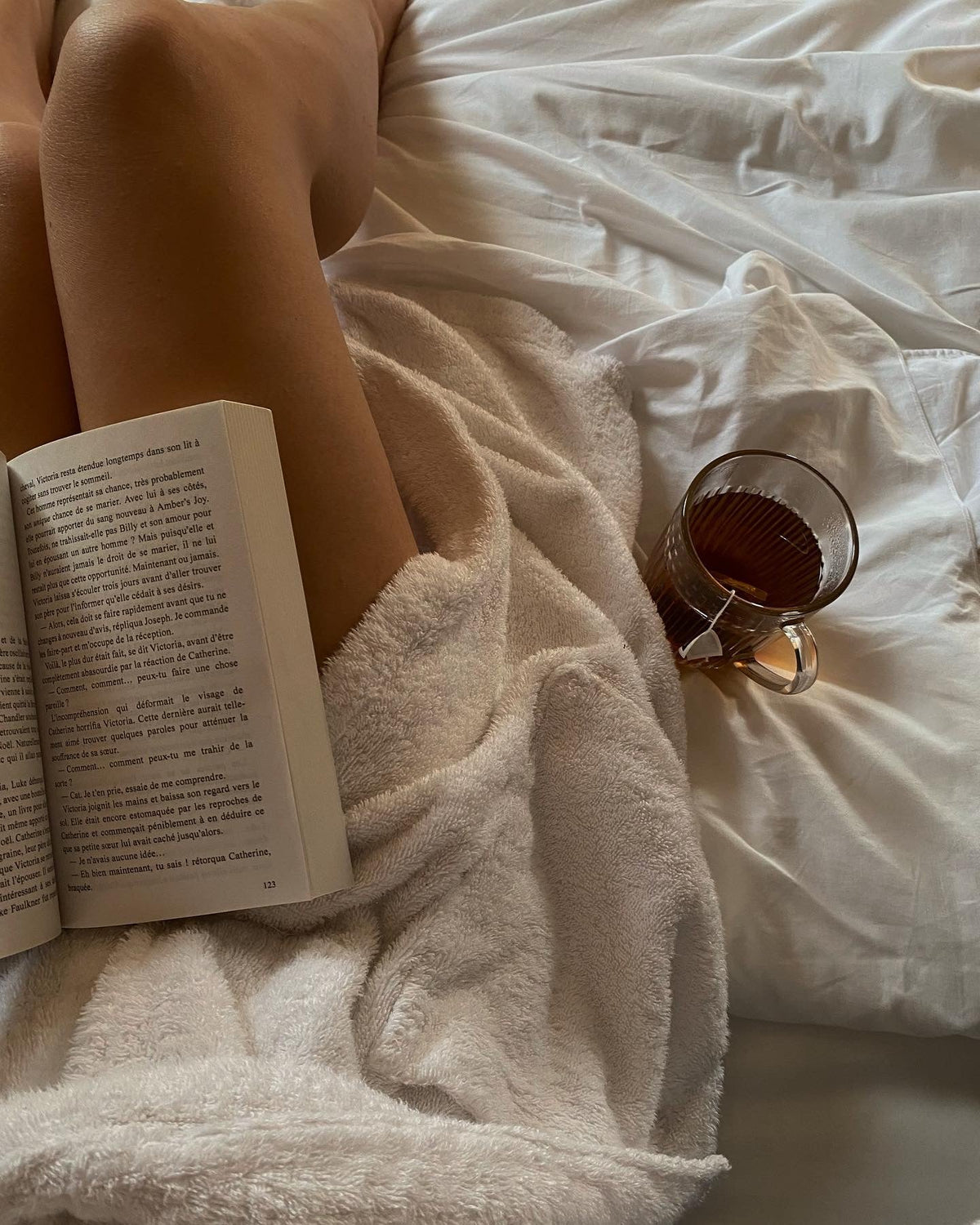 femme lisant un livre dans son lit, avec une infusion