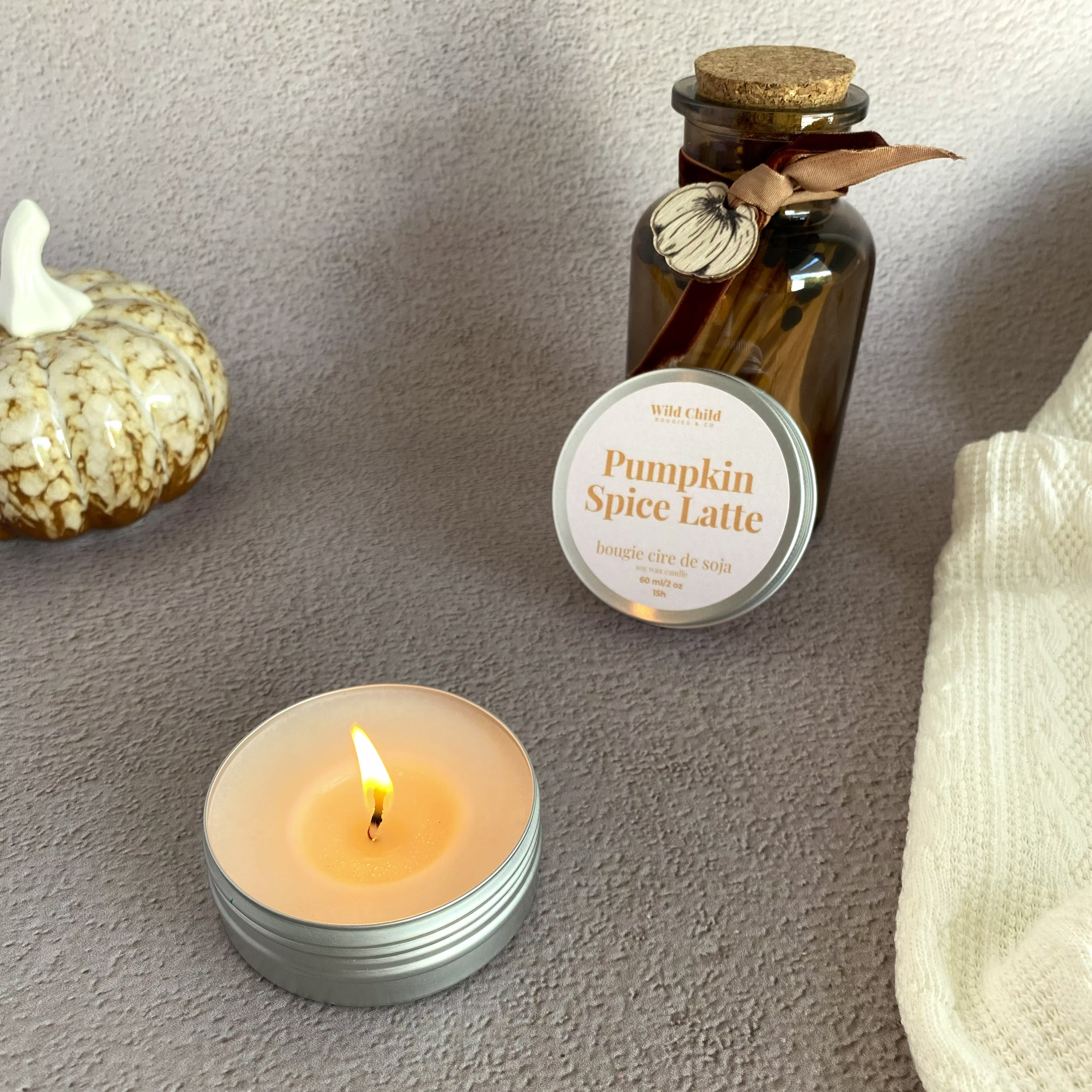 Bougie pumpkin spice latte allumée avec une décoration citrouille et un plaid et des allumettes